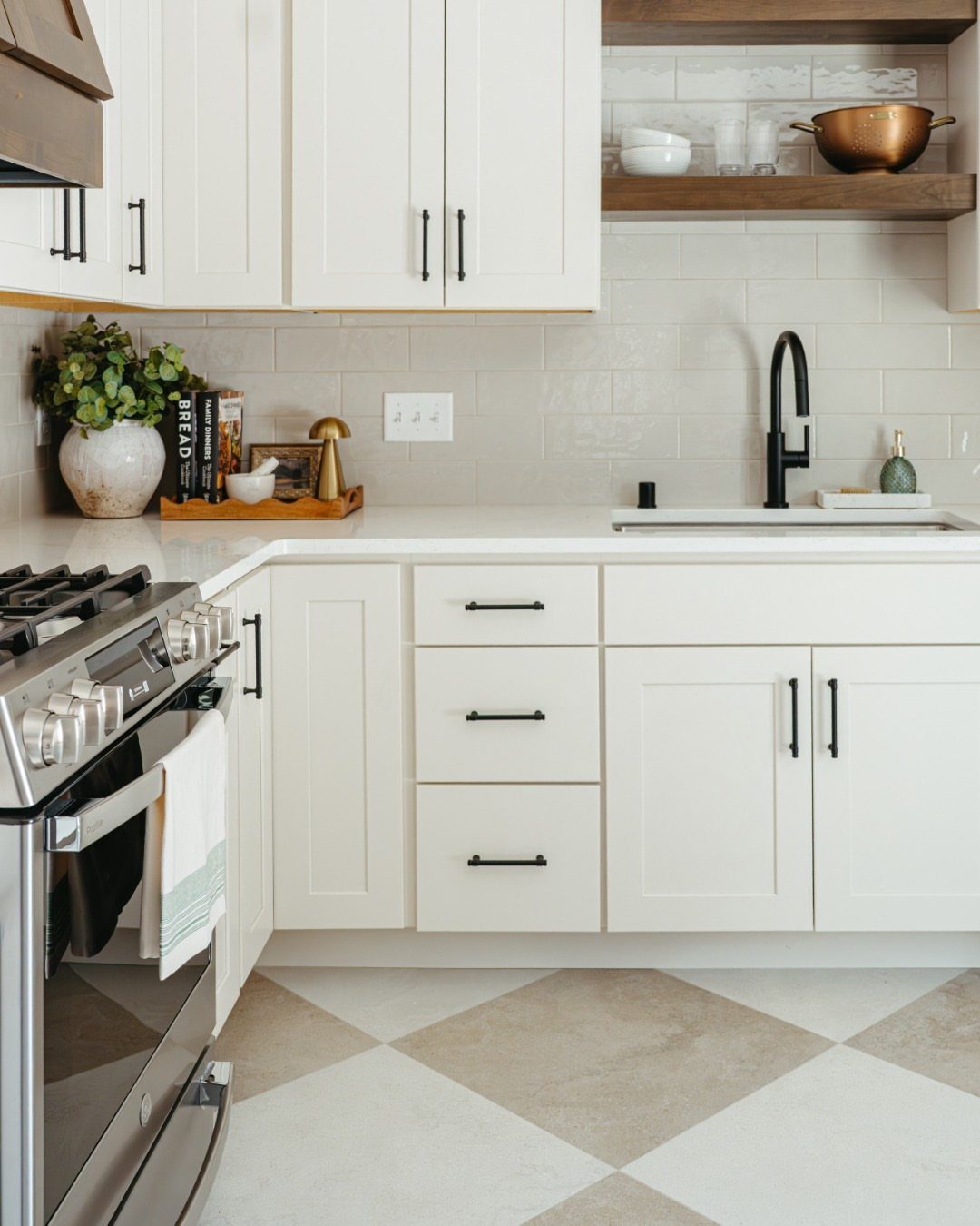 White kitchen cabinets and counters with a large beige and cream checkerboard tile floor.