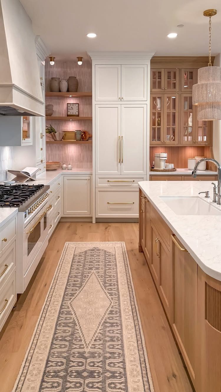 A bright kitchen with light wood cabinets, white marble countertops, and a patterned runner rug.