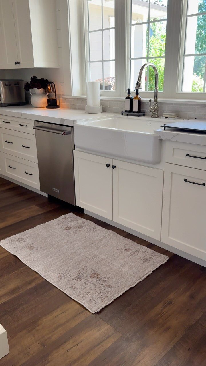 A small vintage patterned rug sits on dark wood kitchen flooring in front of white cabinets.