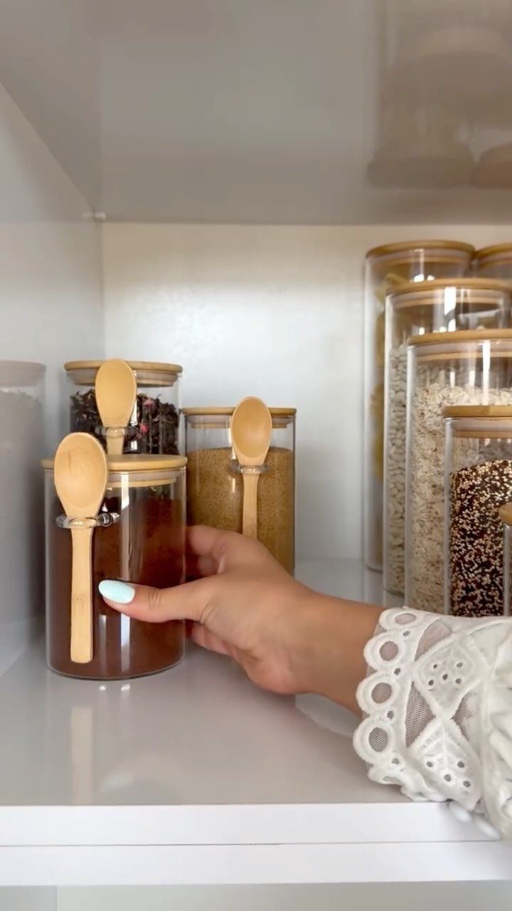 A hand reaches for a glass jar filled with brown spice on a white shelf.