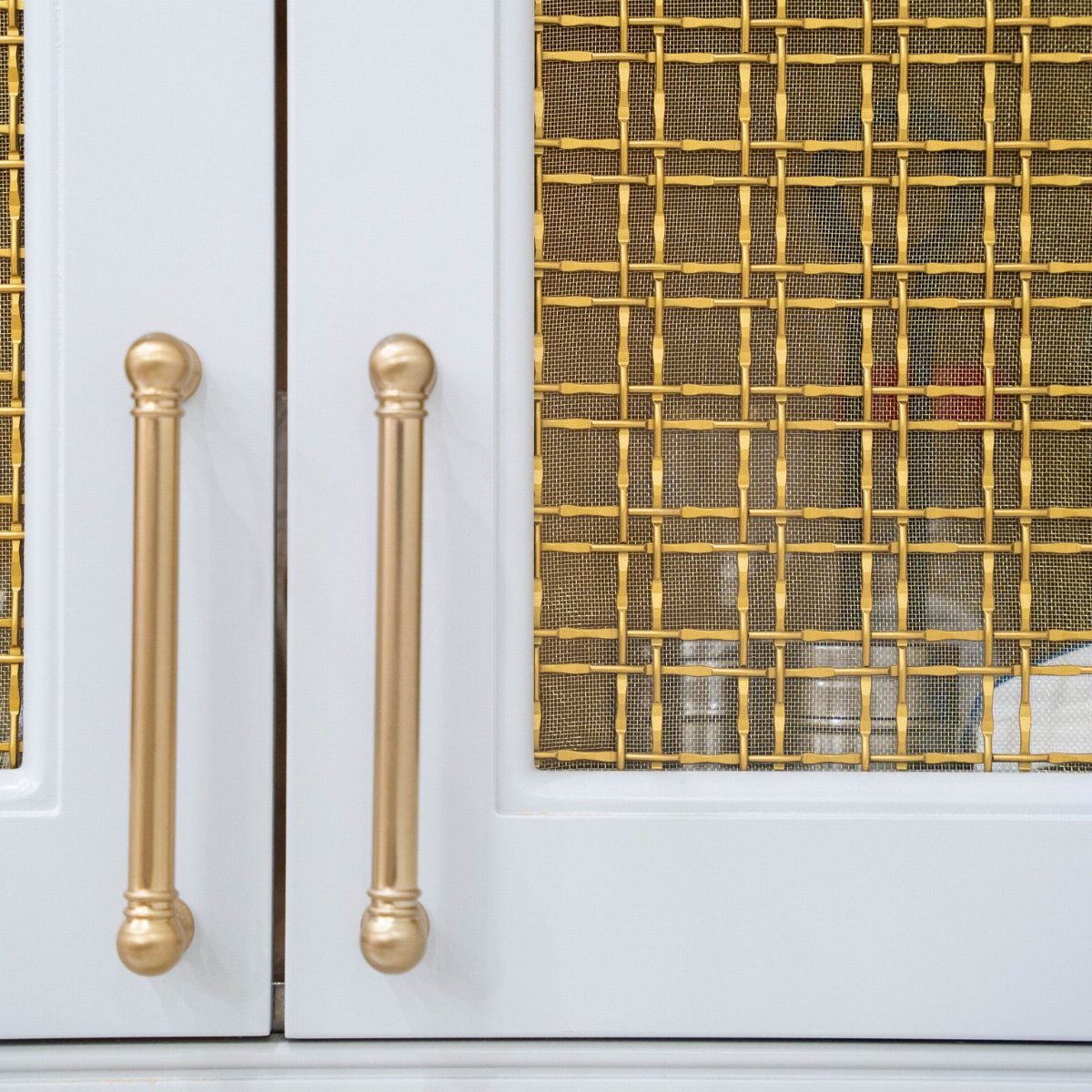 White kitchen cabinets with elegant gold handles and gold mesh wire inserts.