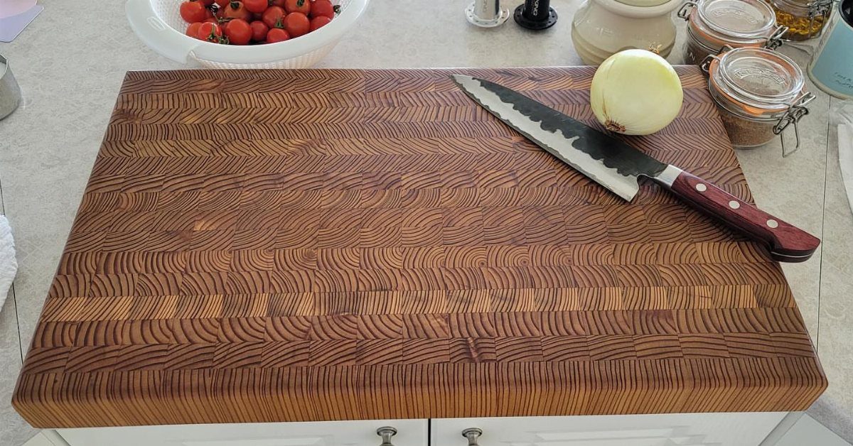 A large wooden cutting board with a chef knife and a white onion on top.