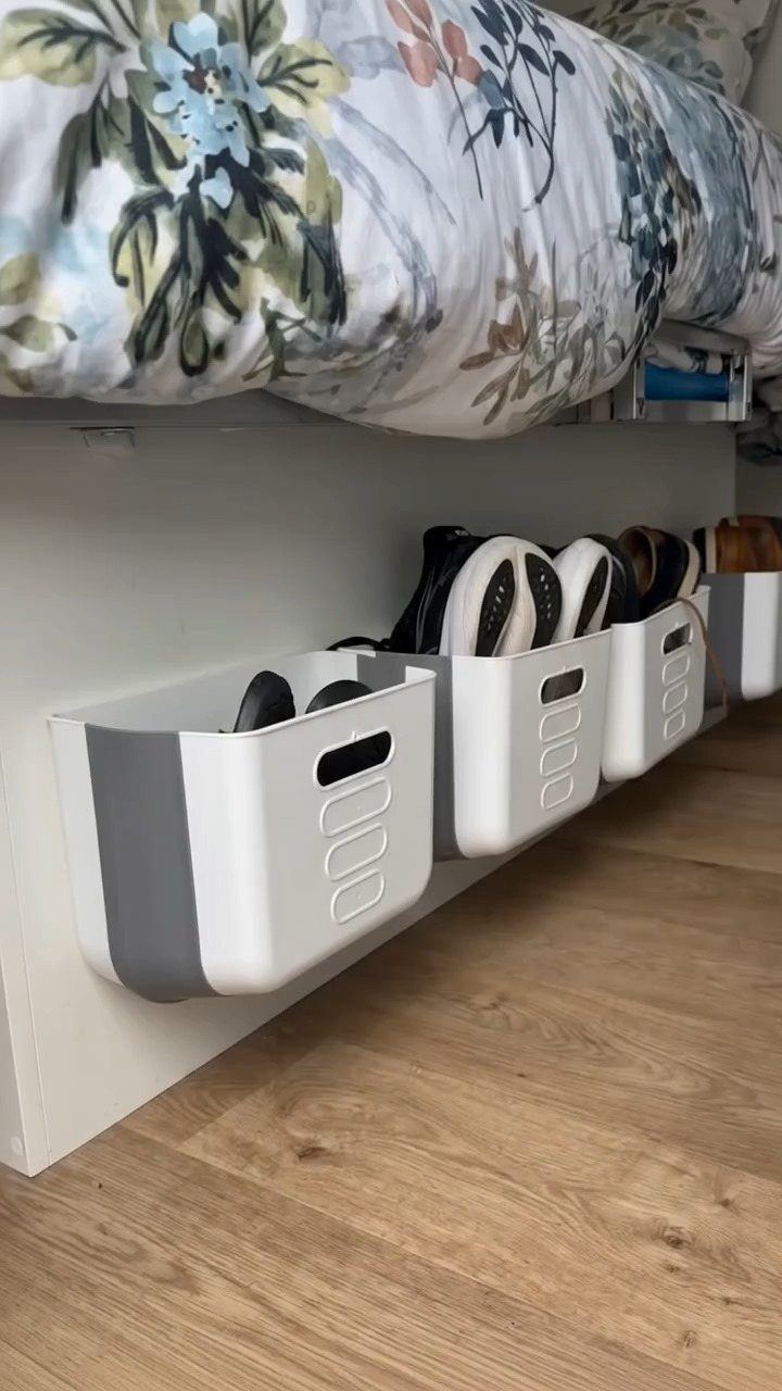 White and grey plastic bins containing shoes mounted on a shelf under a bed.