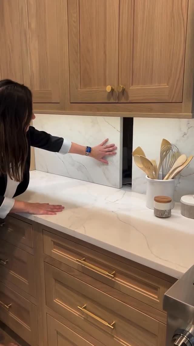 Woman reaching into a narrow appliance garage opening in a marble kitchen backsplash.