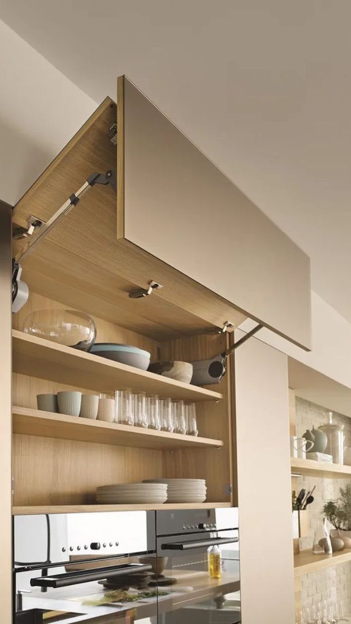 An open wooden kitchen cabinet with bi-fold doors revealing shelves filled with dishes and glassware.