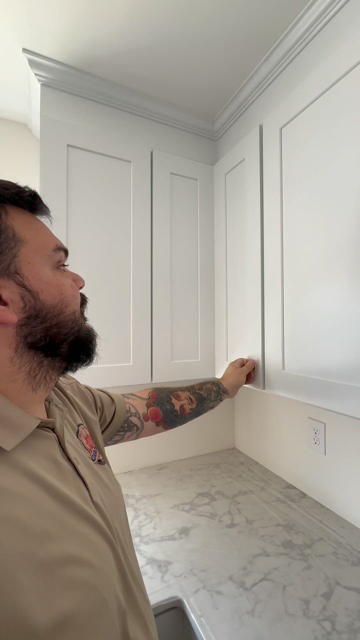 A man installing white shaker-style kitchen cabinets into a corner above a marble countertop.