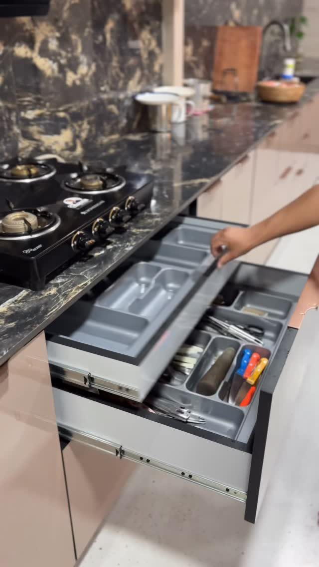 An open kitchen drawer containing a grey organizer filled with various metal utensils and cutlery.