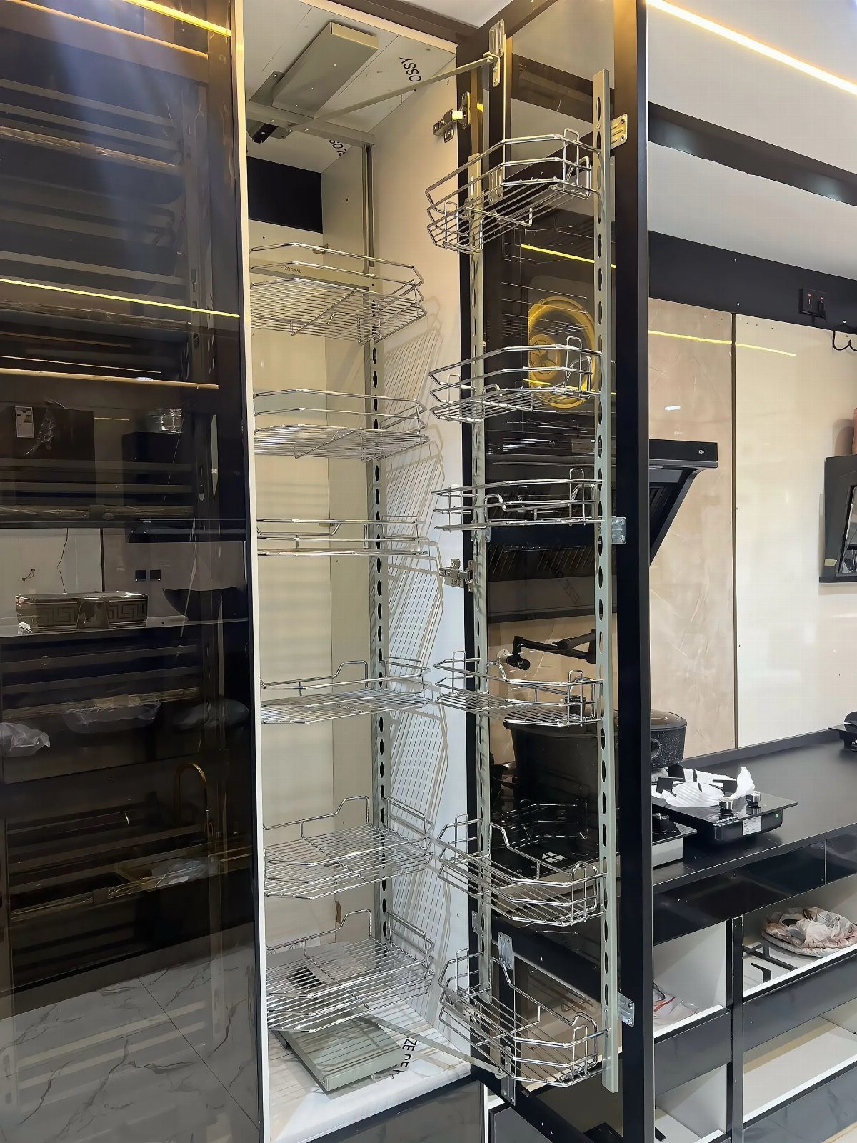 A tall, narrow pull-out pantry cabinet with chrome wire baskets extended in a modern kitchen.