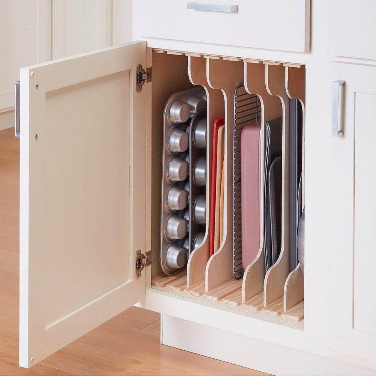 Vertical wooden dividers inside an open white cabinet organizing baking sheets and muffin tins.