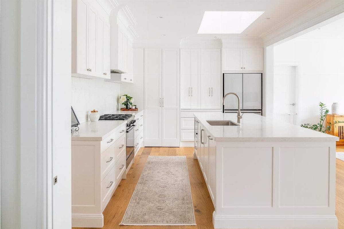 White kitchen cabinets with a large central island and light wood flooring under a skylight.