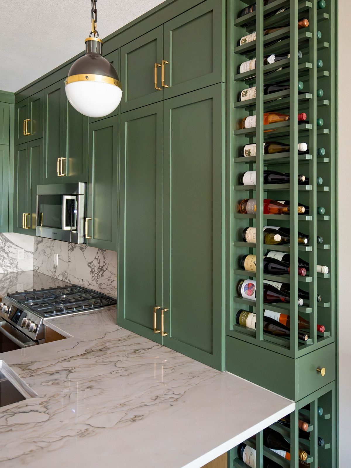 Sage green kitchen cabinets featuring a built-in vertical wine rack and marble countertops.