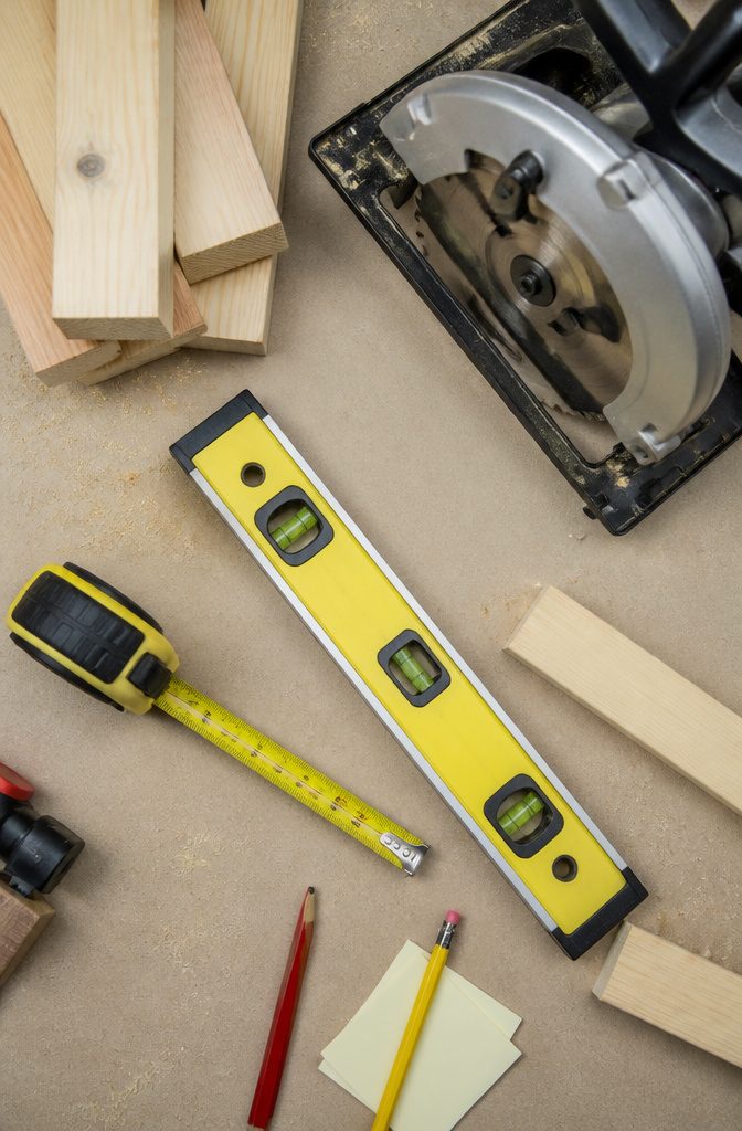 A measuring tape, level, and stud finder on a work surface.