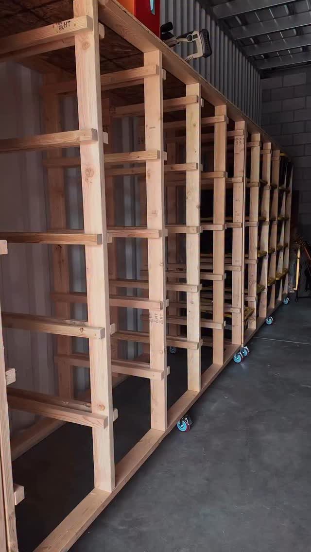 A long, custom-built wooden shelving unit on wheels standing in a garage or workshop.