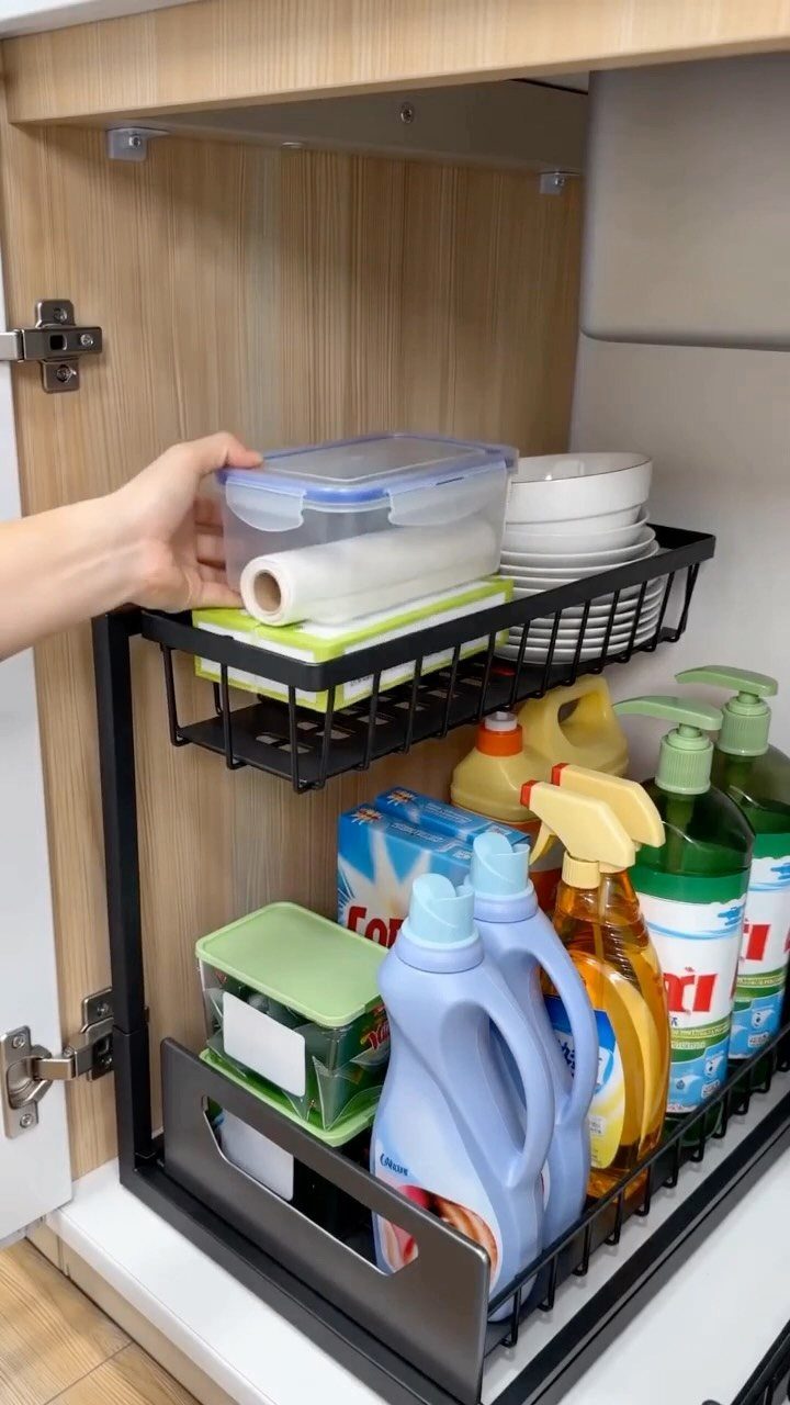 A hand reaches for a plastic container on a black pull-out wire shelf inside a cabinet.