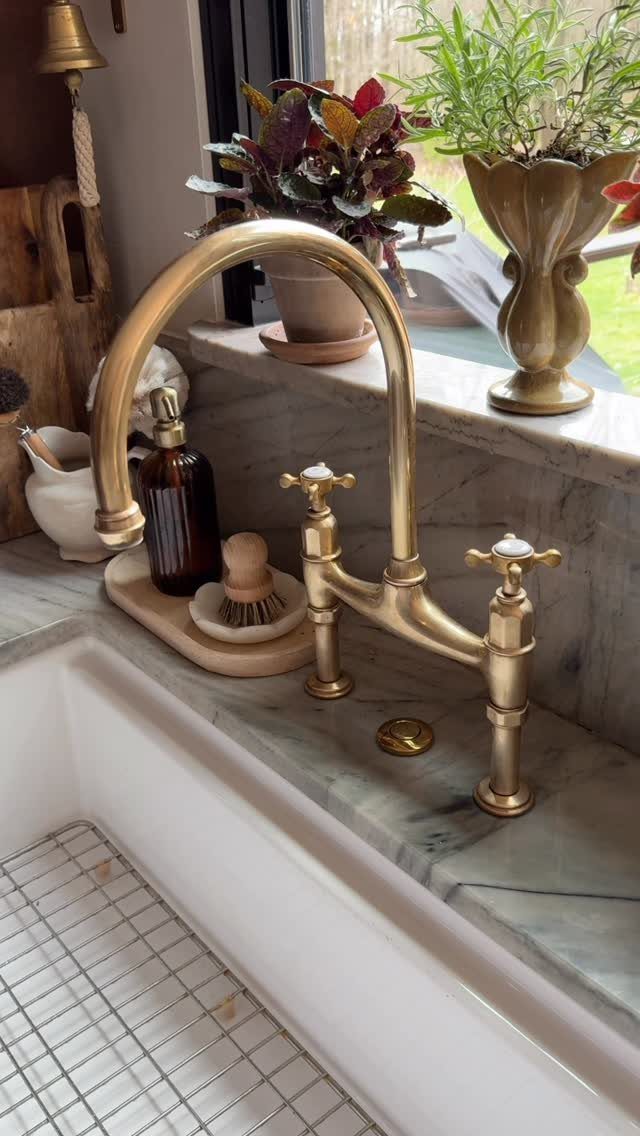 A brass kitchen faucet with two handles sits on a marble countertop by a white sink.