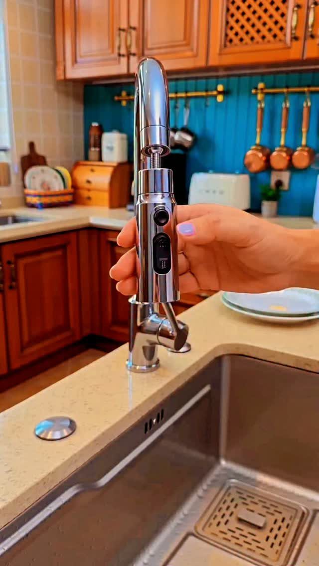 A hand touching a shiny chrome kitchen faucet installed on a countertop near a sink.