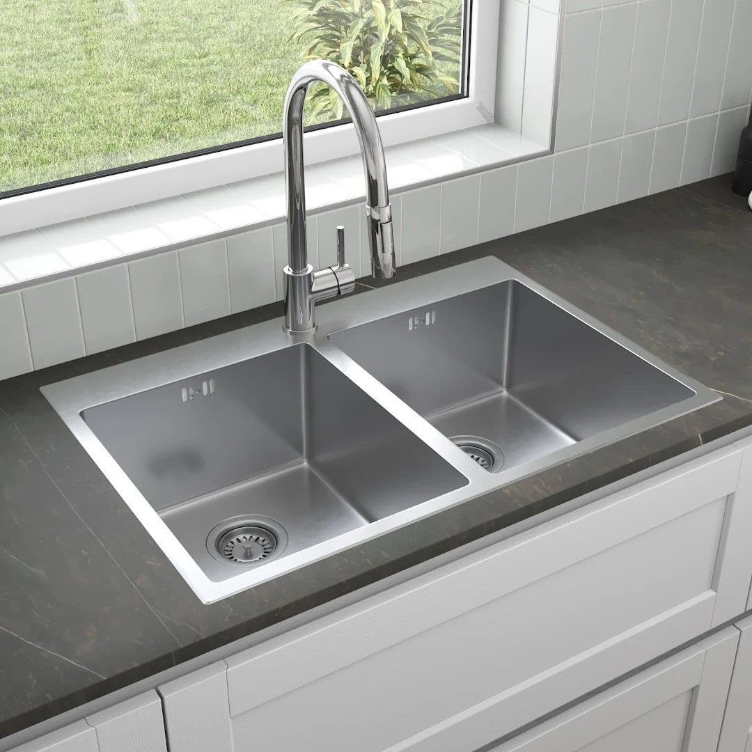 Stainless steel double bowl kitchen sink with a chrome faucet installed in a dark countertop.