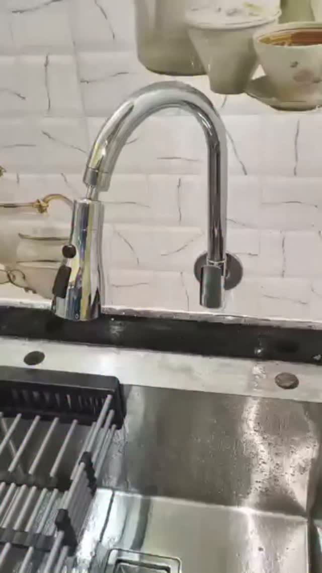 A chrome wall-mounted kitchen faucet with a pull-out sprayer over a stainless steel sink.