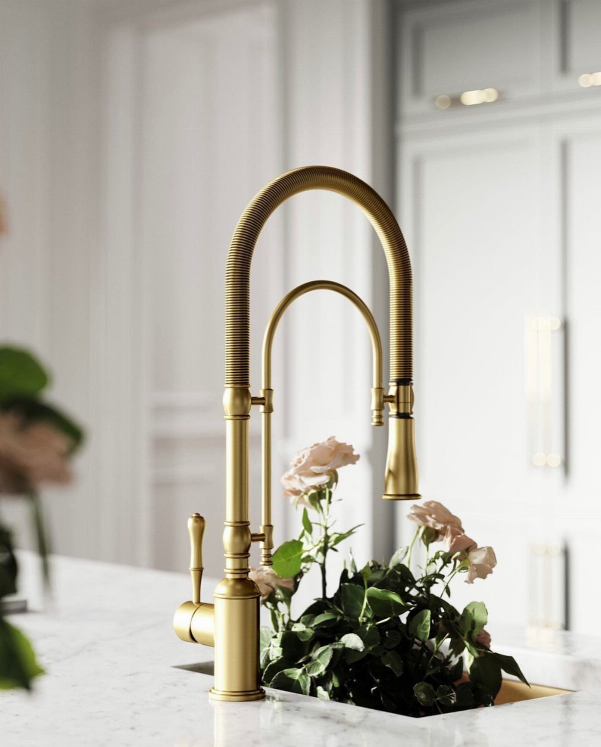 A gold coiled spring kitchen faucet sits on a white marble countertop near pink roses.