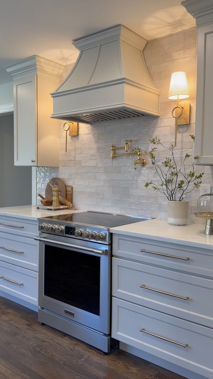 White kitchen cabinets with gold hardware, a stainless steel stove, and a large white range hood.