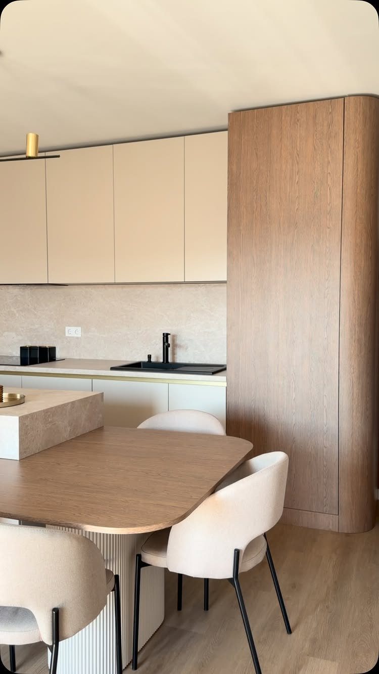 Beige kitchen cabinets and light wood furniture in a neutral toned modern dining area.