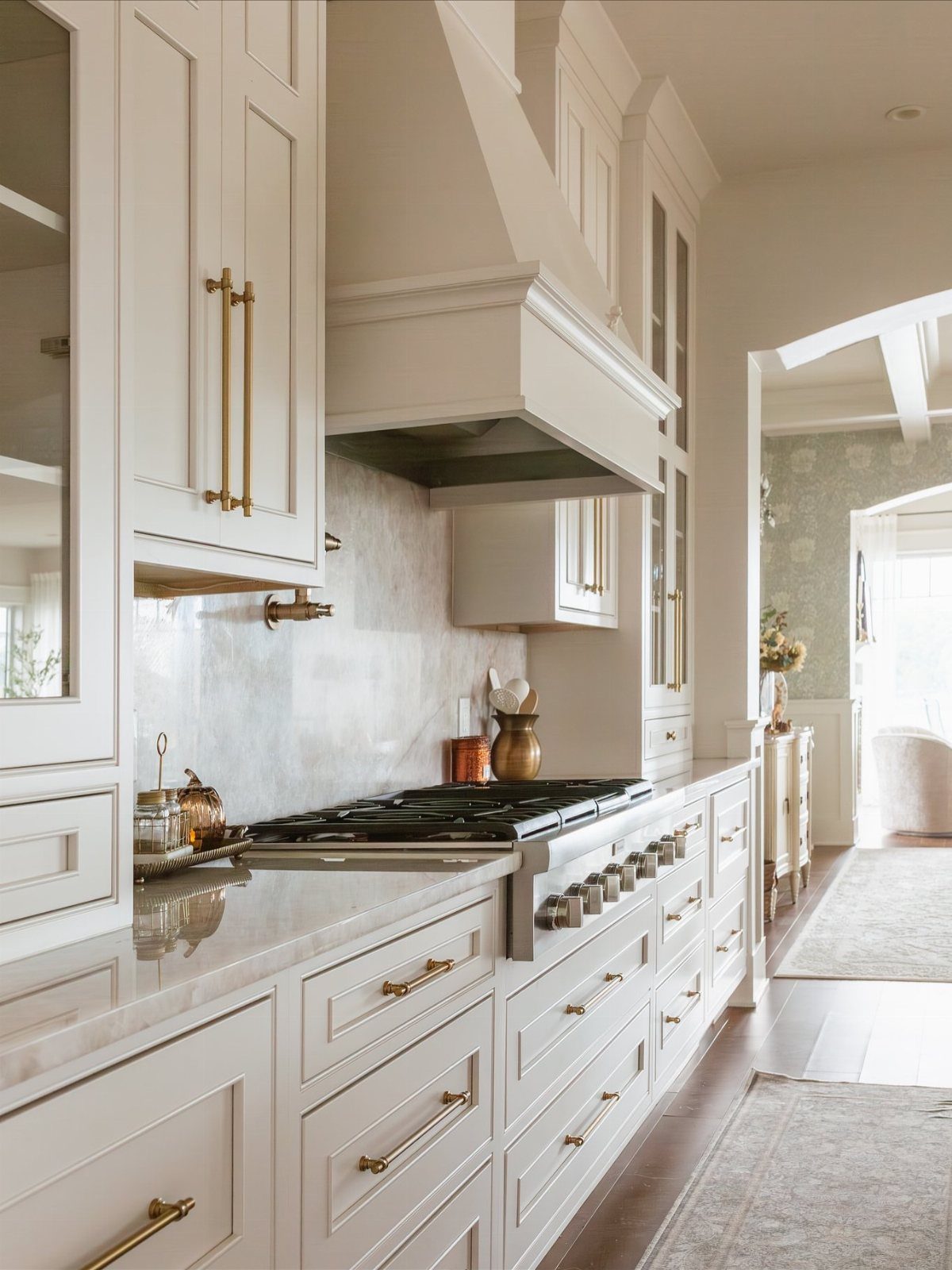 Cream Shaker-style kitchen cabinets with marble countertops and gold hardware surrounding a large stove.