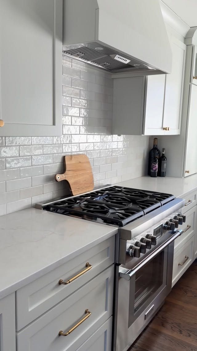 White subway tile backsplash installed behind a stainless steel stove and light grey kitchen cabinets.