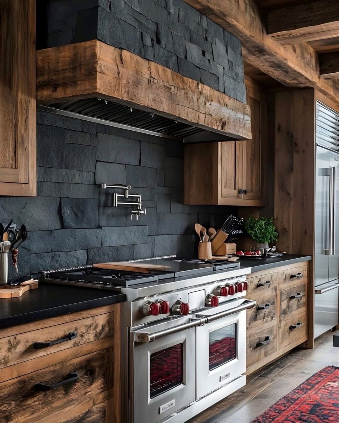 Black natural stone tiles covering a kitchen backsplash behind a stainless steel stove and wooden cabinets.
