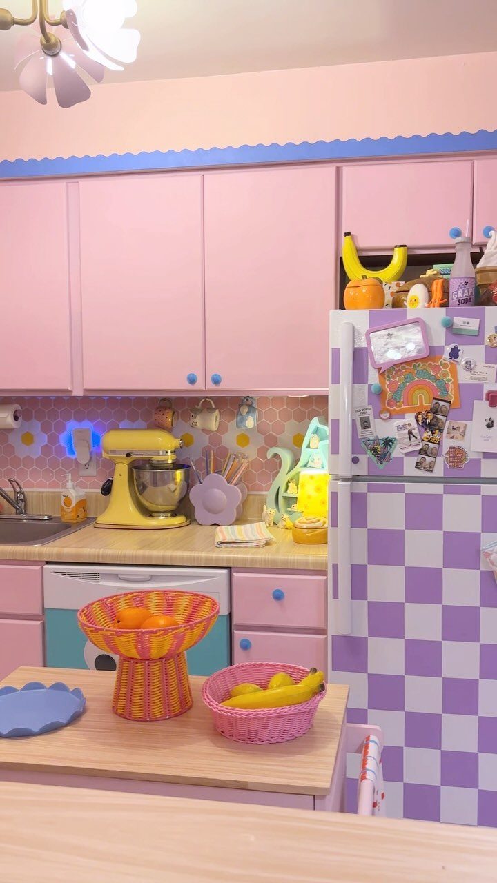Pink kitchen with pastel cabinets, a checkered refrigerator, and a floral daisy pattern backsplash.