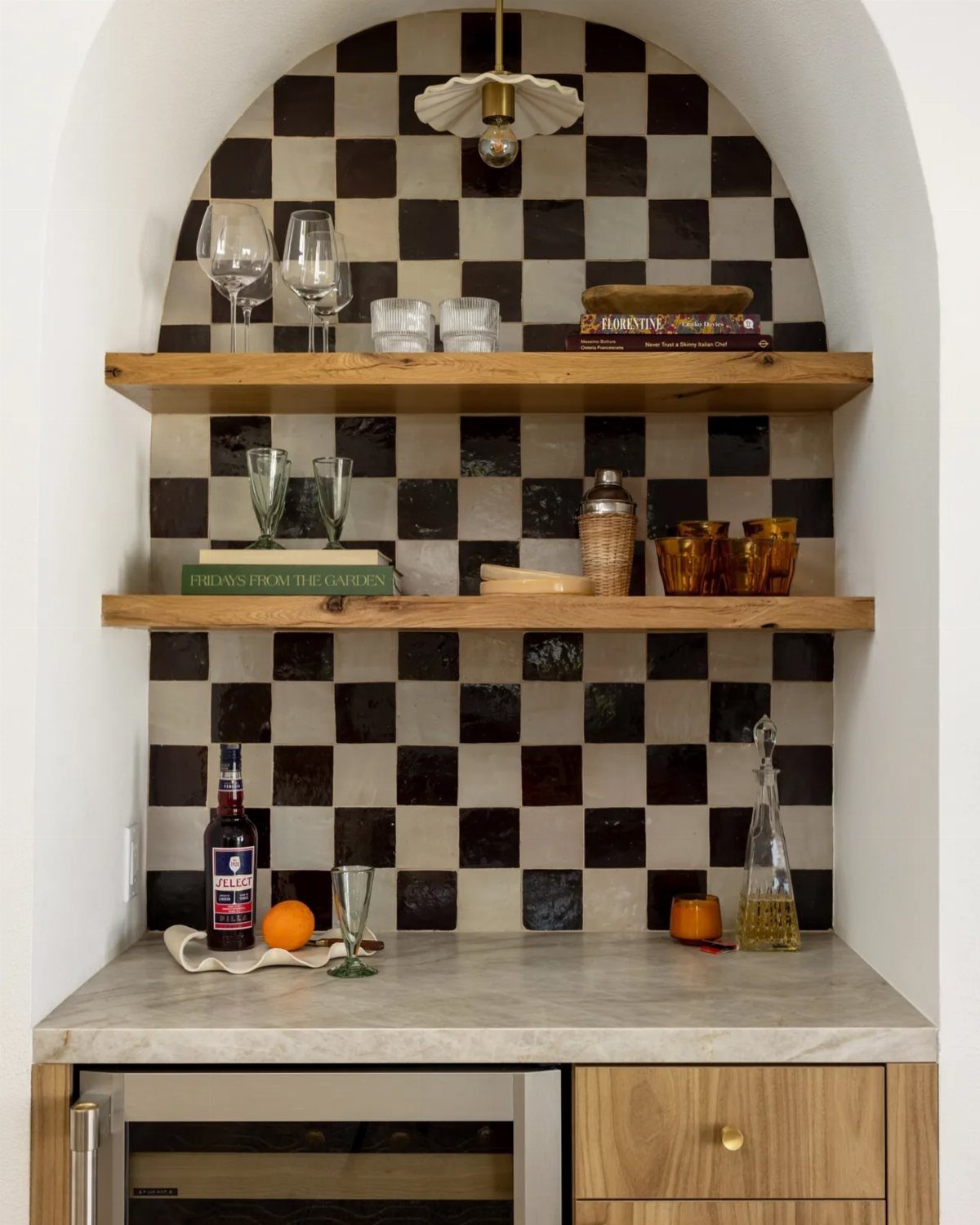 Checkerboard pattern backsplash with dark and light tiles inside a white arched kitchen alcove.