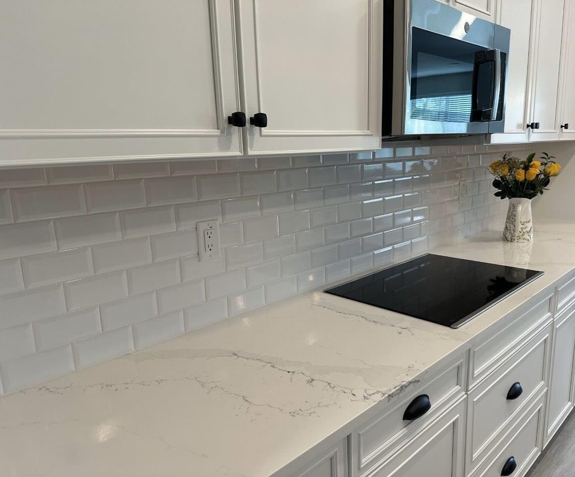 White glossy subway tiles installed as a backsplash above a white marble kitchen countertop.