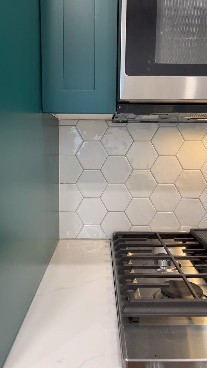 White hexagonal tiles installed as a kitchen backsplash between teal cabinets and a white countertop.