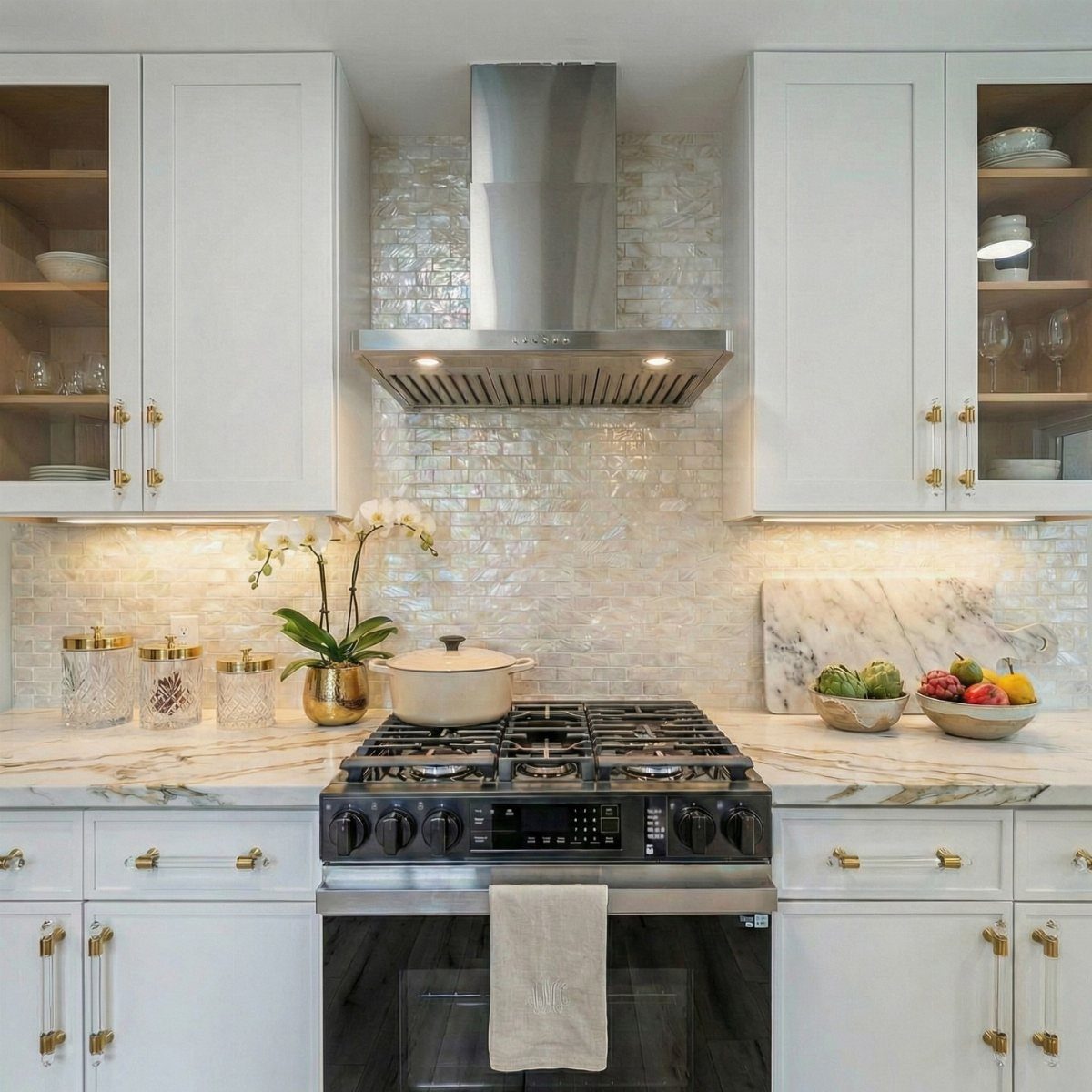 Iridescent mosaic tiles covering a kitchen backsplash between white cabinets and a stainless steel stove.