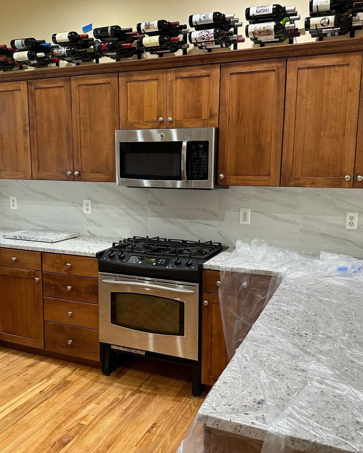Large marble-patterned tiles installed as a kitchen backsplash between wooden cabinets and granite countertops.
