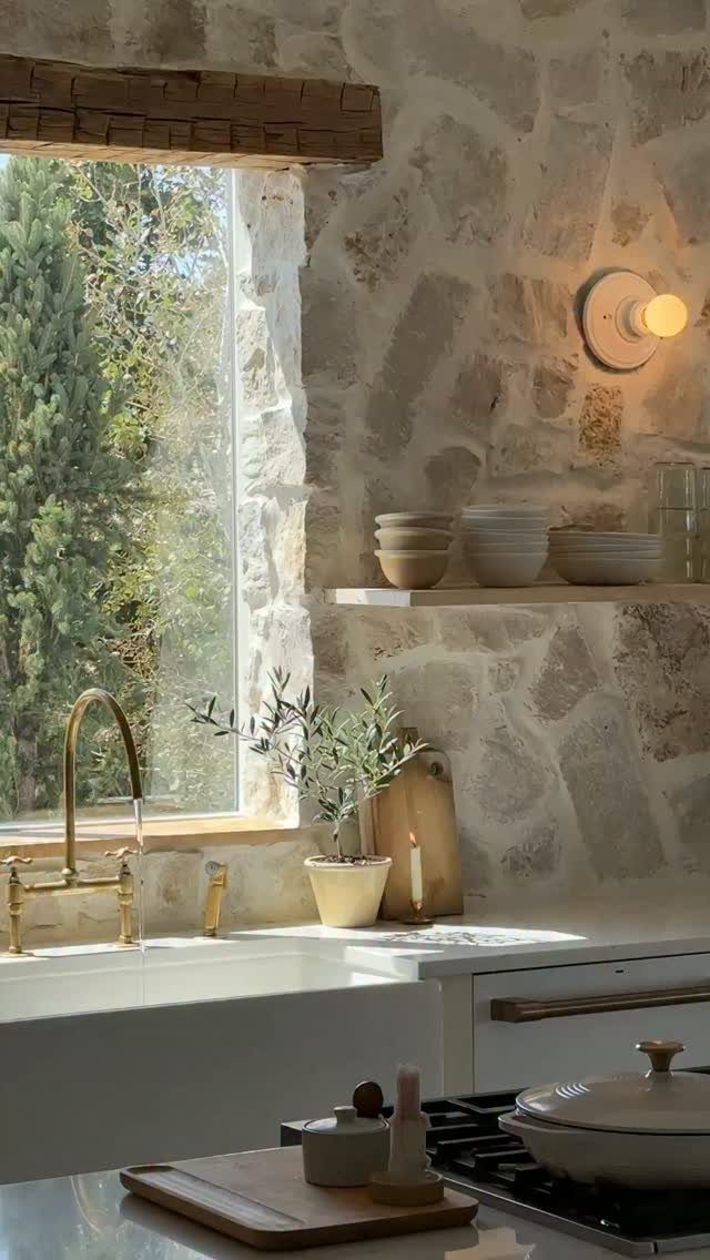 Natural light-colored stone wall used as a kitchen backsplash next to a window.