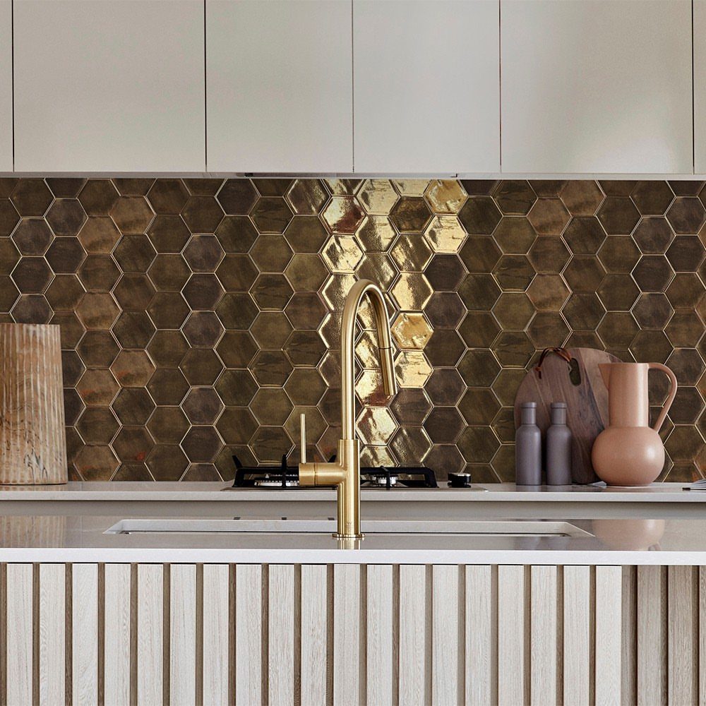 Gold metallic hexagonal tiles covering a kitchen backsplash behind a brass faucet and white countertop.
