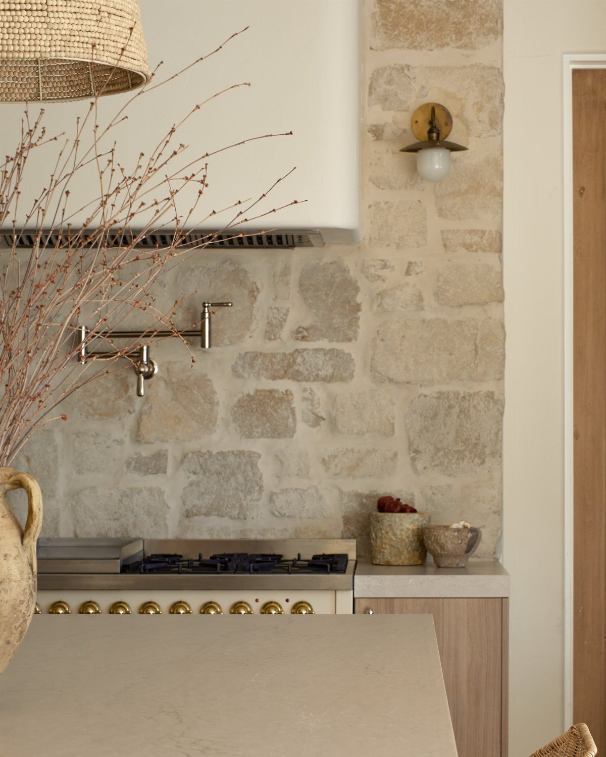 Natural stone blocks forming a textured backsplash behind a stainless steel kitchen stove and pot filler.