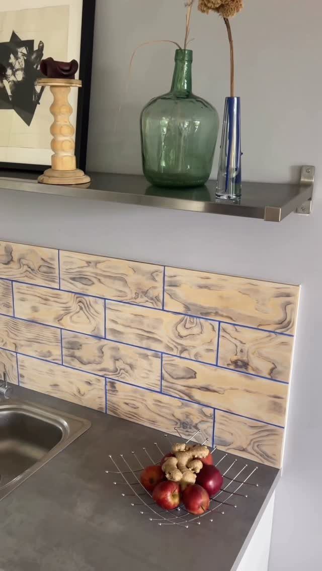 Wood grain patterned backsplash tiles with blue grout lines above a grey kitchen countertop.